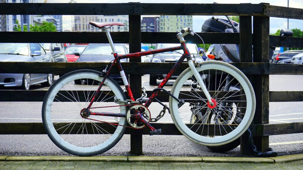 A vibrant bicycle locked to a wooden railing in a city parking lot with background cars.
